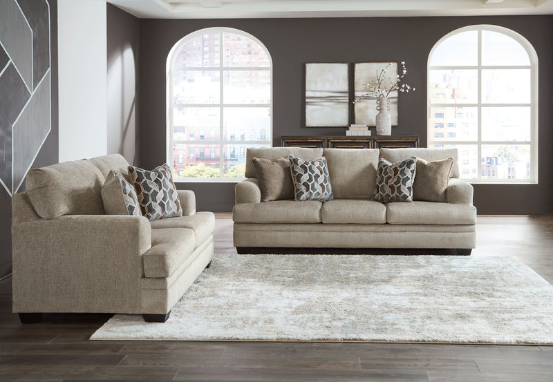 Taupe fabric sofa set with chaise chair and ottoman, arranged around a large area rug.