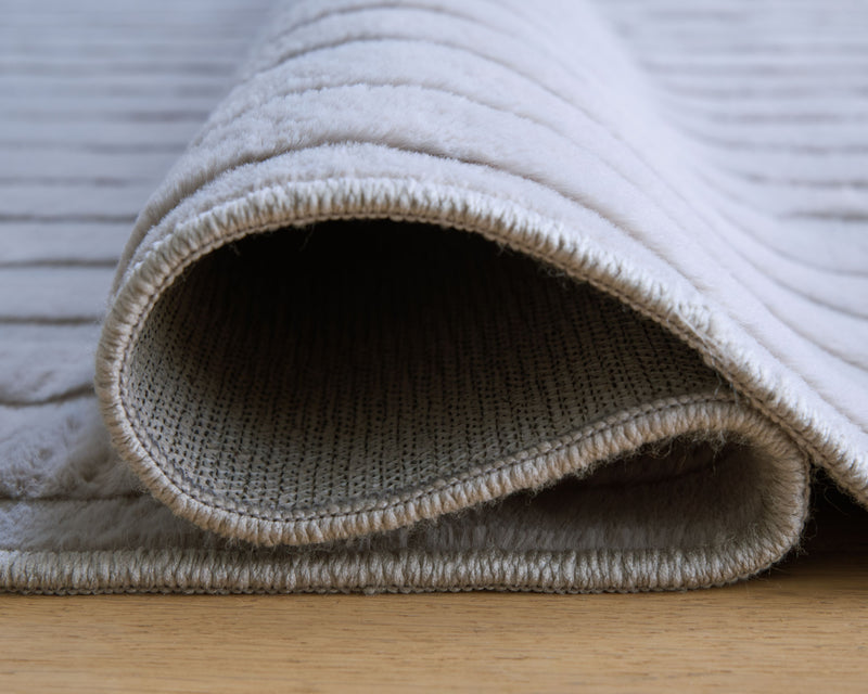 Light gray washable rug, rolled edge showing textured loops and stitched border