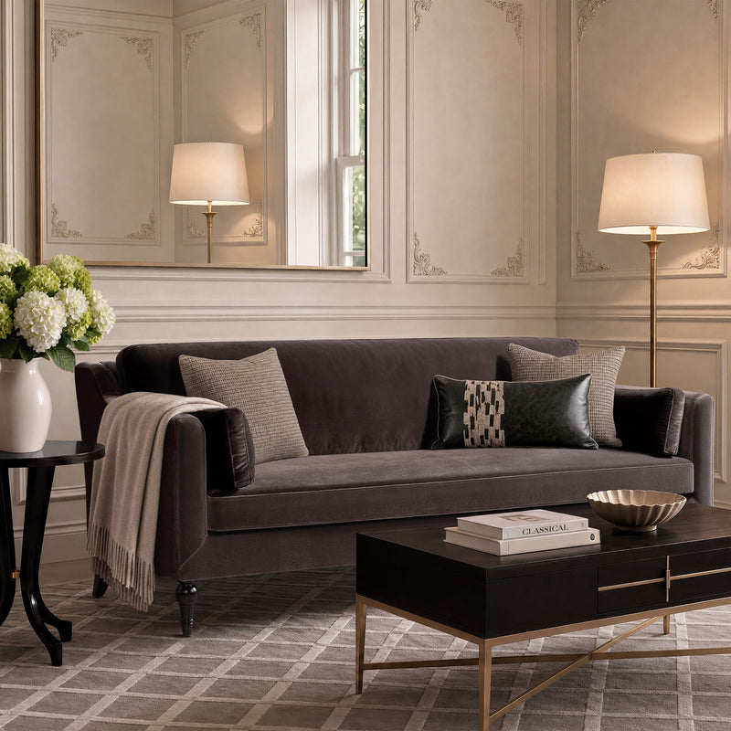Dark brown upholstered modern sofa with two accent pillows and a draped throw blanket