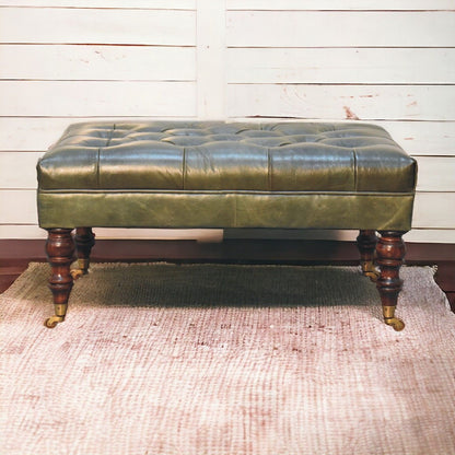 Dark green leather ottoman with tufted top and wooden castor legs