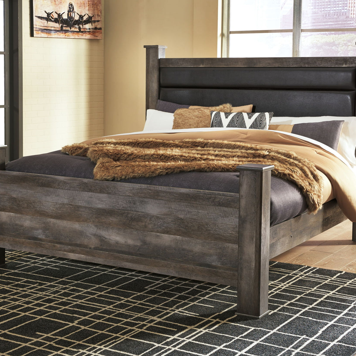 Gray upholstered poster bed with dark headboard, styled with quilt, blanket, and pillows