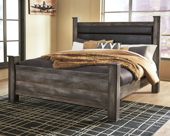 Gray upholstered poster bed with dark headboard, styled with quilt, blanket, and pillows