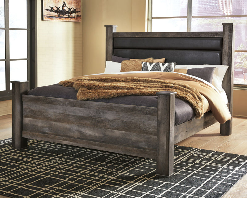 Gray upholstered poster bed with dark headboard, styled with quilt, blanket, and pillows