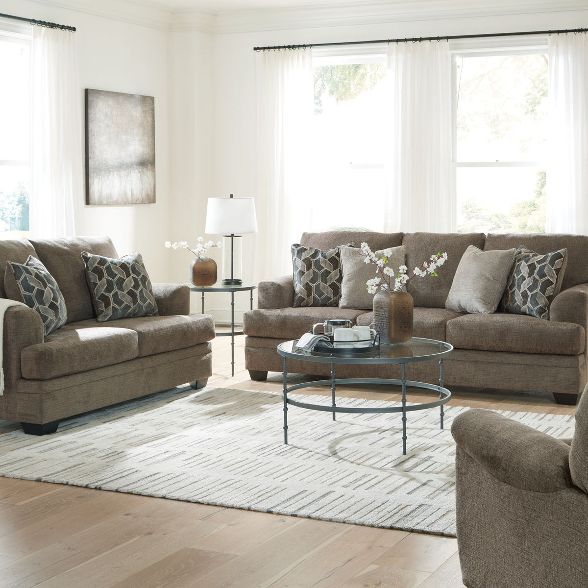 Taupe fabric living room sofa set with chair and ottoman, shown with pillows and throw blankets.