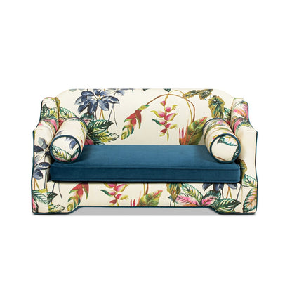 Dog sofa bed with botanical floral cover, blue cushion, and rounded arm bolsters