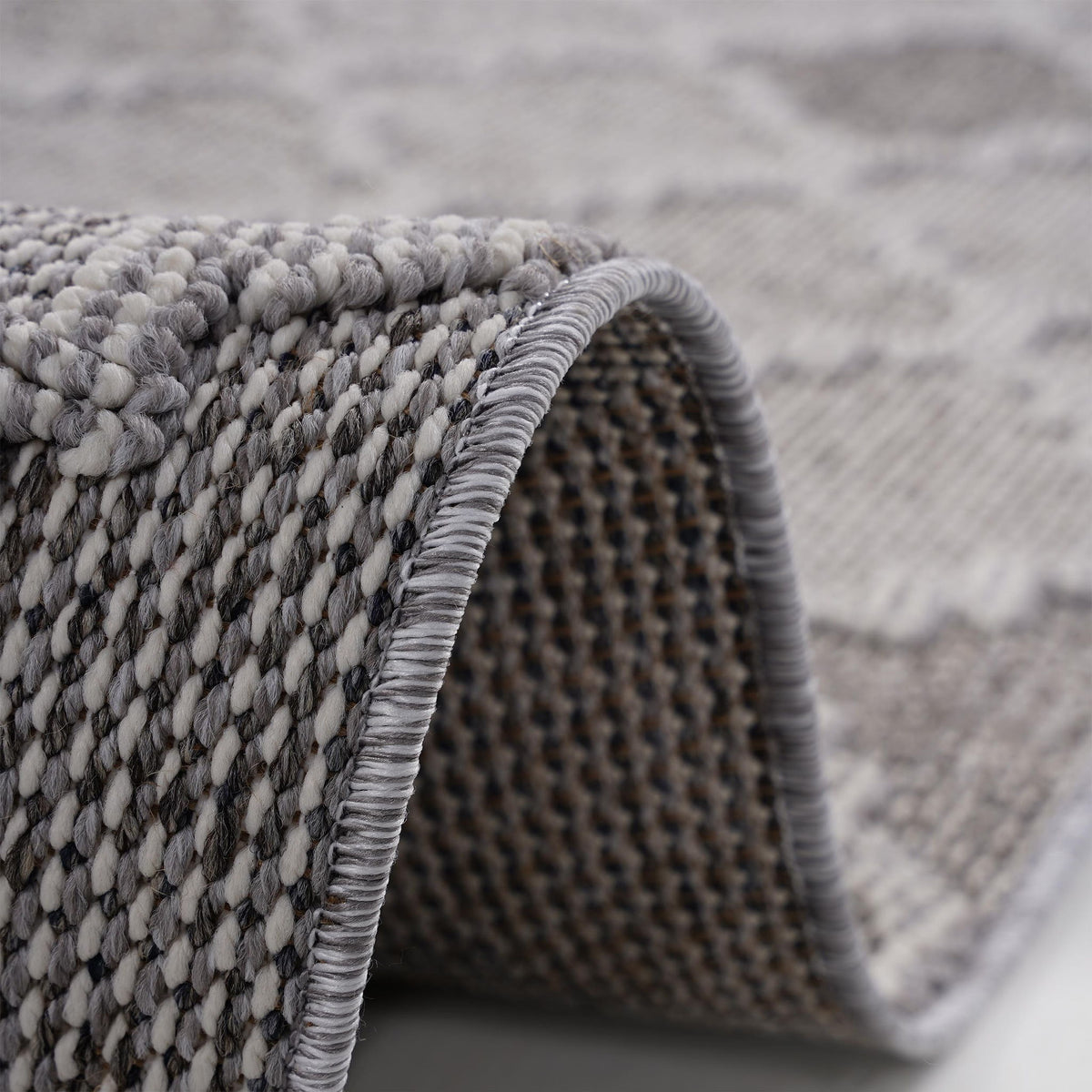 Corner close-up of gray trellis area rug with textured pile and stitched edge