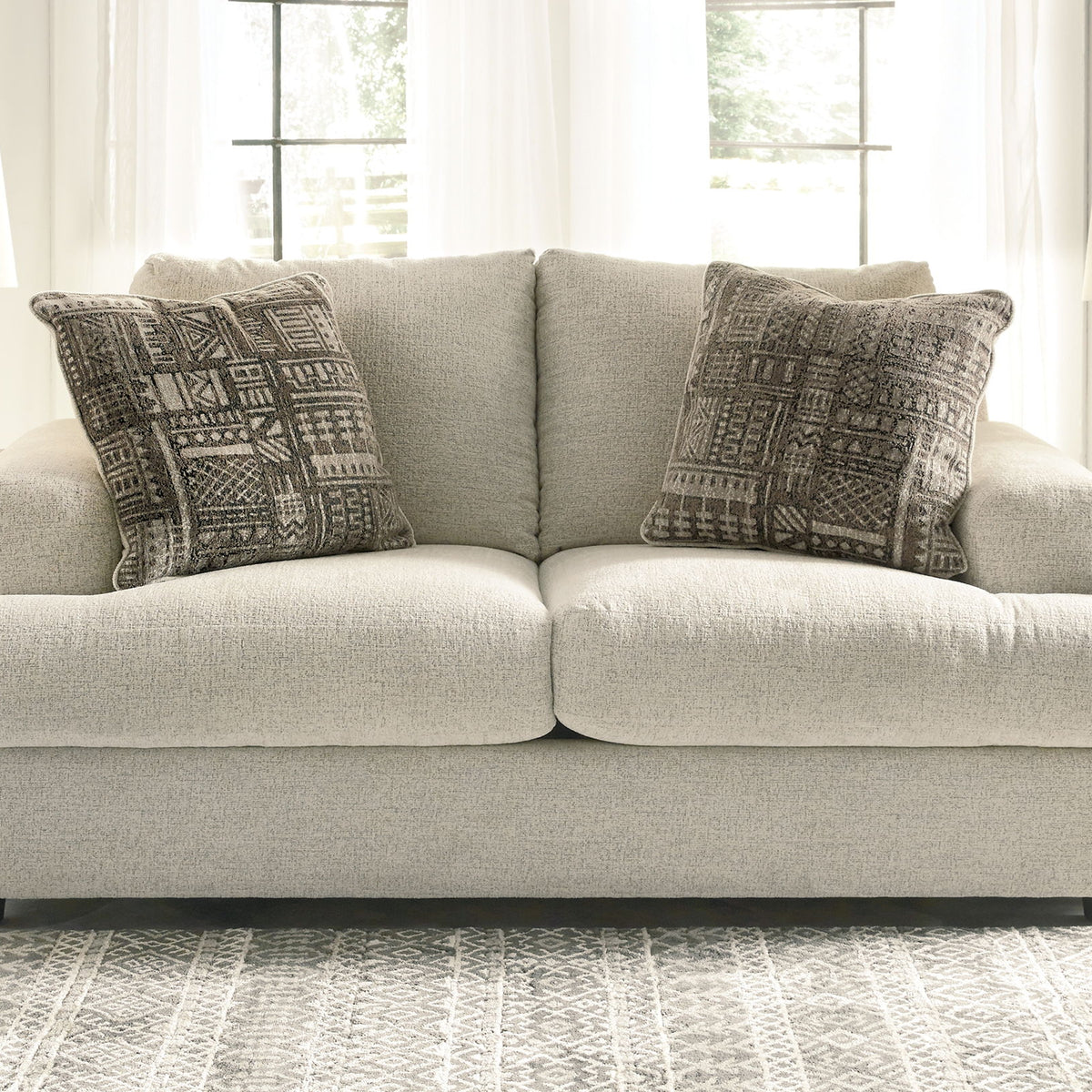 Stone gray loveseat with two dark patterned accent pillows, front view