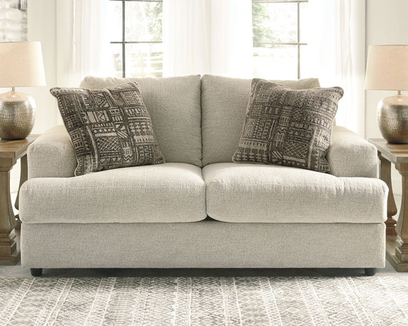 Stone gray loveseat with two dark patterned accent pillows, front view