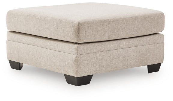Beige upholstered accent ottoman with square top, stacked panels, and dark legs
