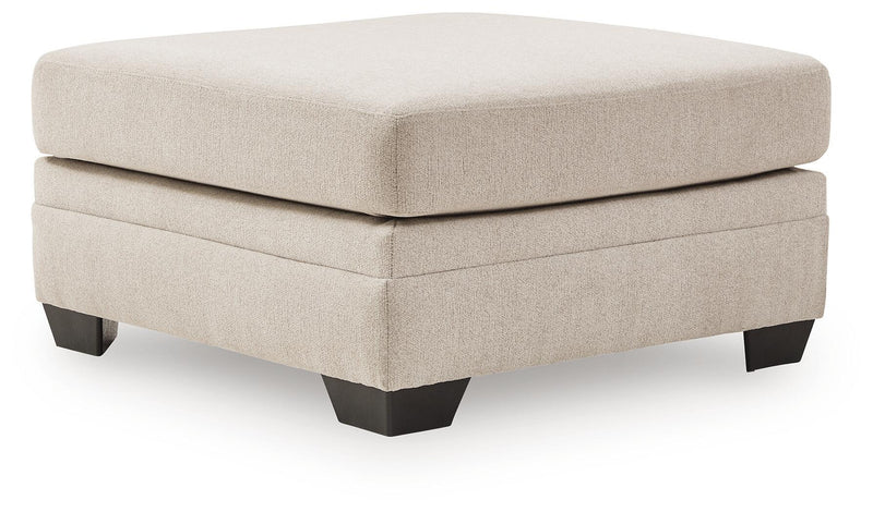 Beige upholstered accent ottoman with square top, stacked panels, and dark legs