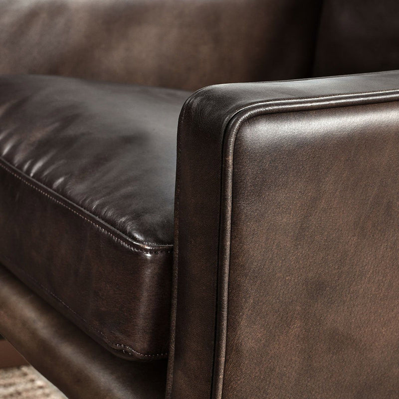 Truffle-brown leather arm and seat cushion with stitched piping, dark frame.