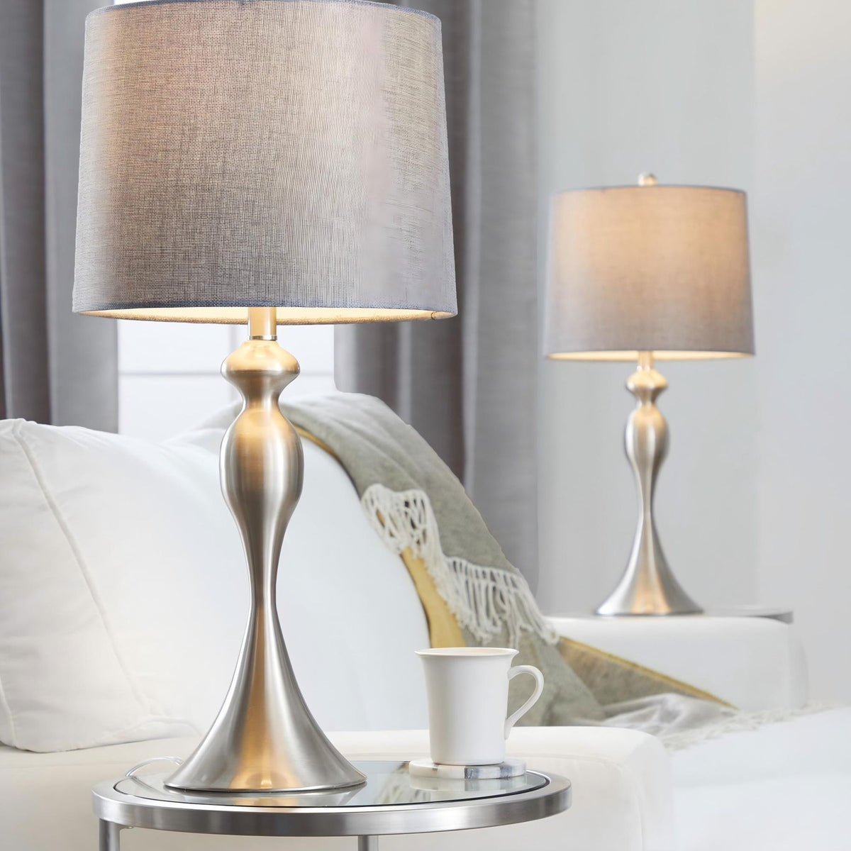 Contemporary table lamp set with tan fabric shades and silver-toned bases on a sofa