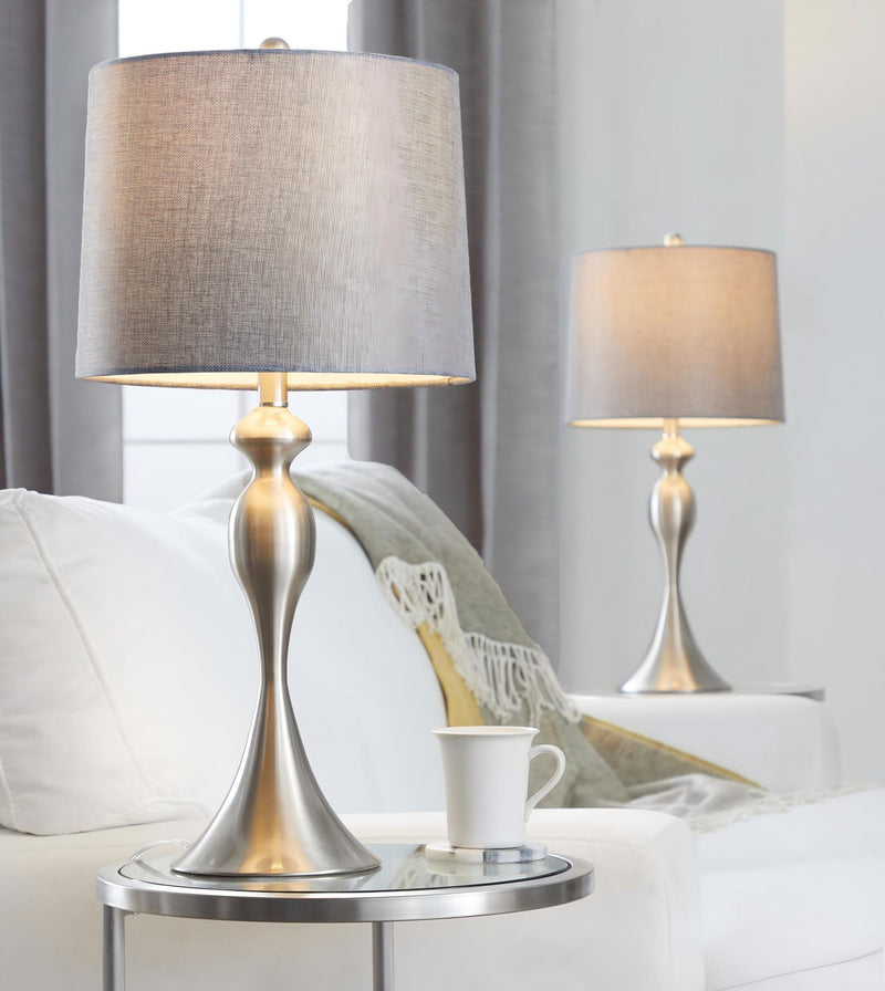 Contemporary table lamp set with tan fabric shades and silver-toned bases on a sofa