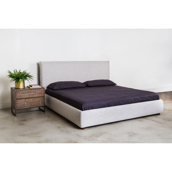 Light gray king bed with dark comforter and two pillows, upholstered headboard