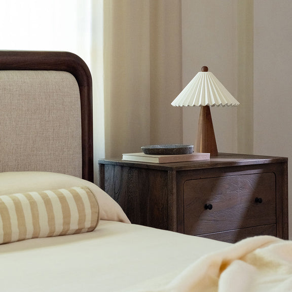 Queen bed with curved brown wood headboard, beige upholstery, and side view
