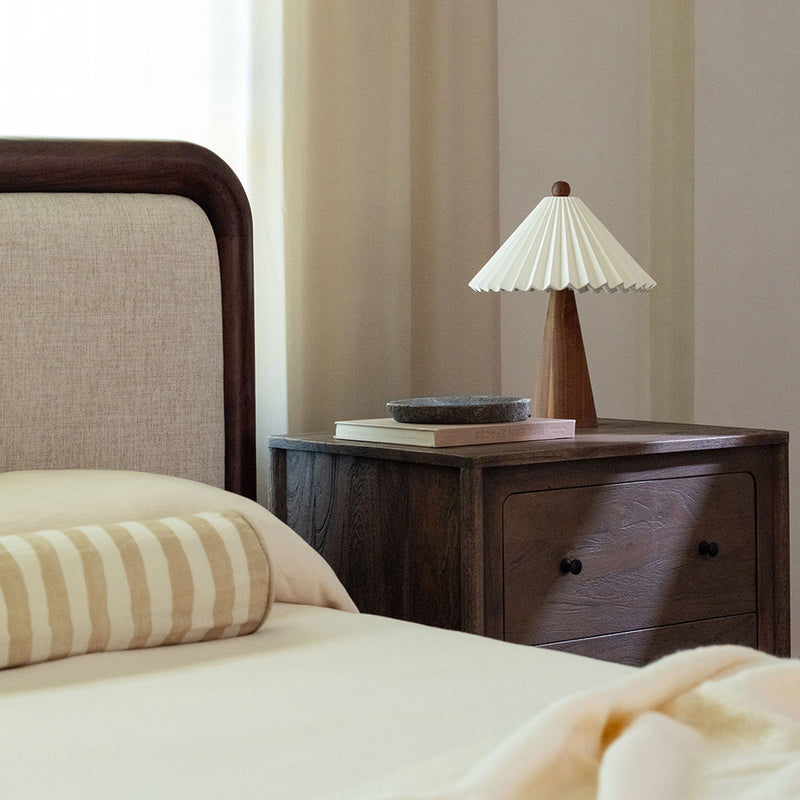 Queen bed with curved brown wood headboard, beige upholstery, and side view