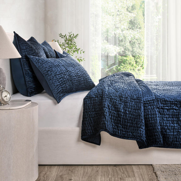 Navy velvet quilt with matching pillows on a bed