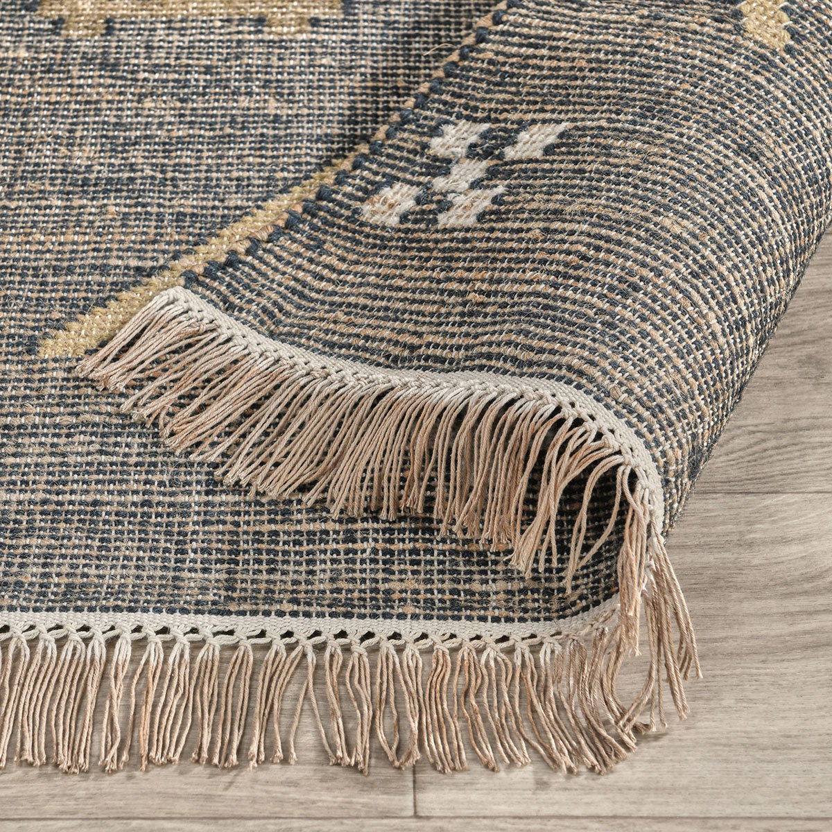 Close-up of dark blue woven area rug corner with fringe trim and geometric motif detail