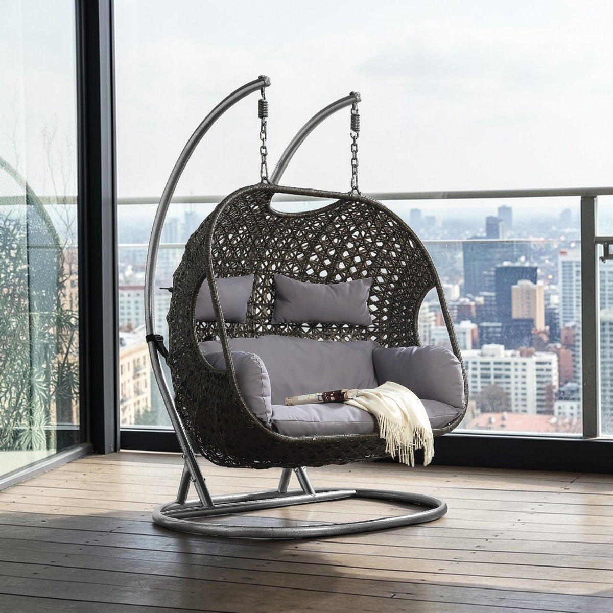 Hanging wicker chair on circular base with light gray cushions and throw pillow