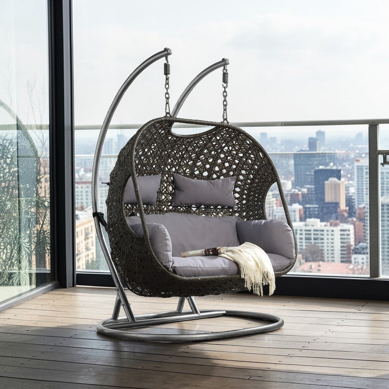 Hanging wicker chair on circular base with light gray cushions and throw pillow