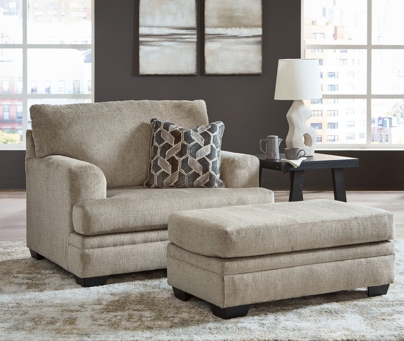 Taupe fabric loveseat with square arms and matching ottoman, styled with patterned throw pillow.