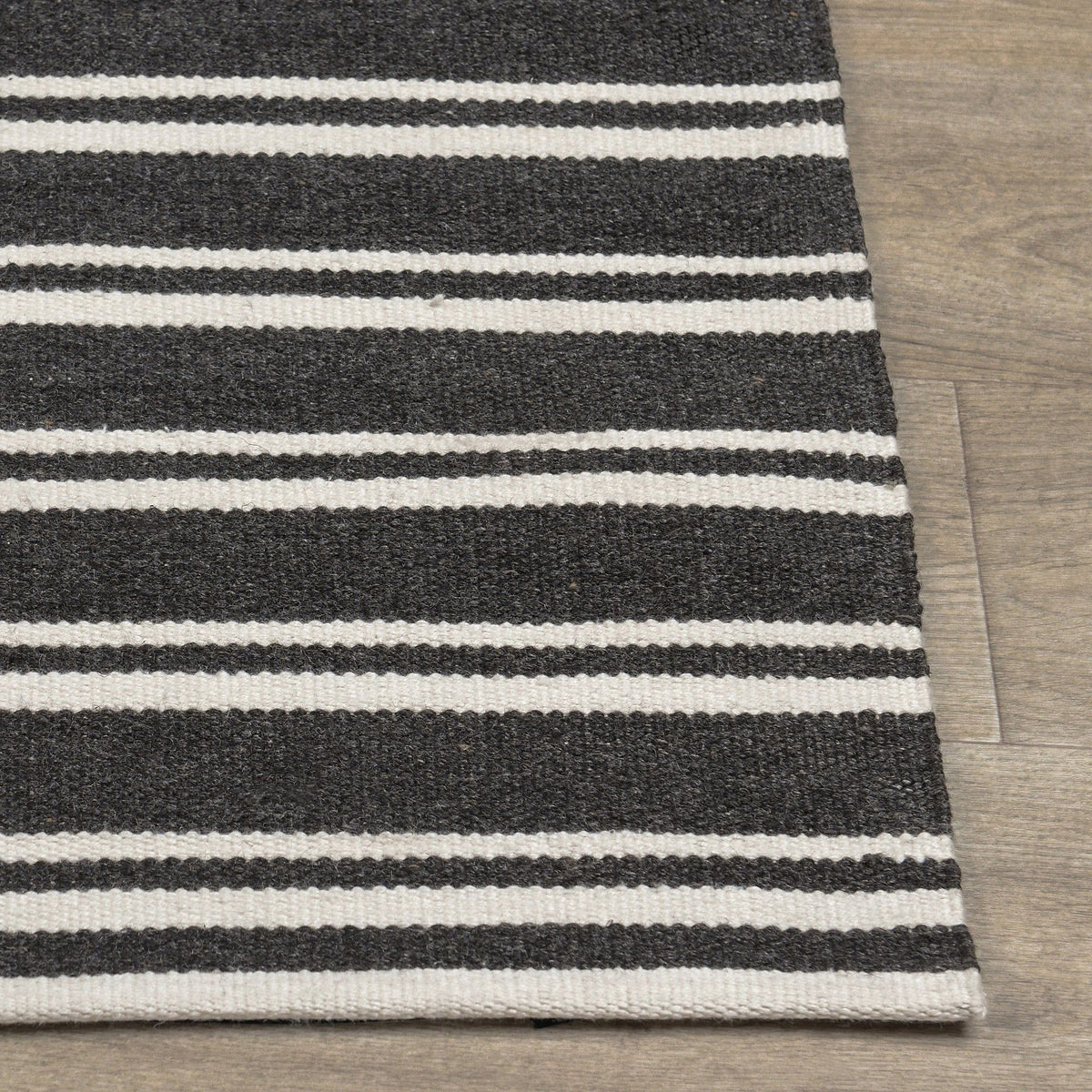 Corner view of charcoal and white striped rug with flat weave and stitched edge