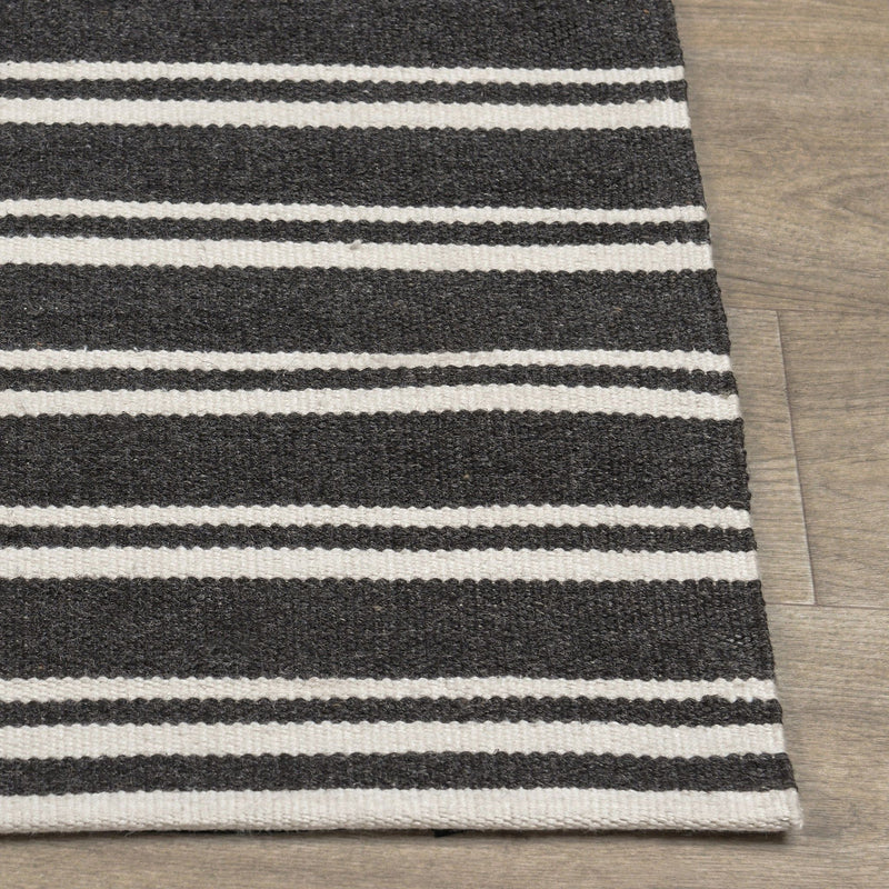 Corner view of charcoal and white striped rug with flat weave and stitched edge