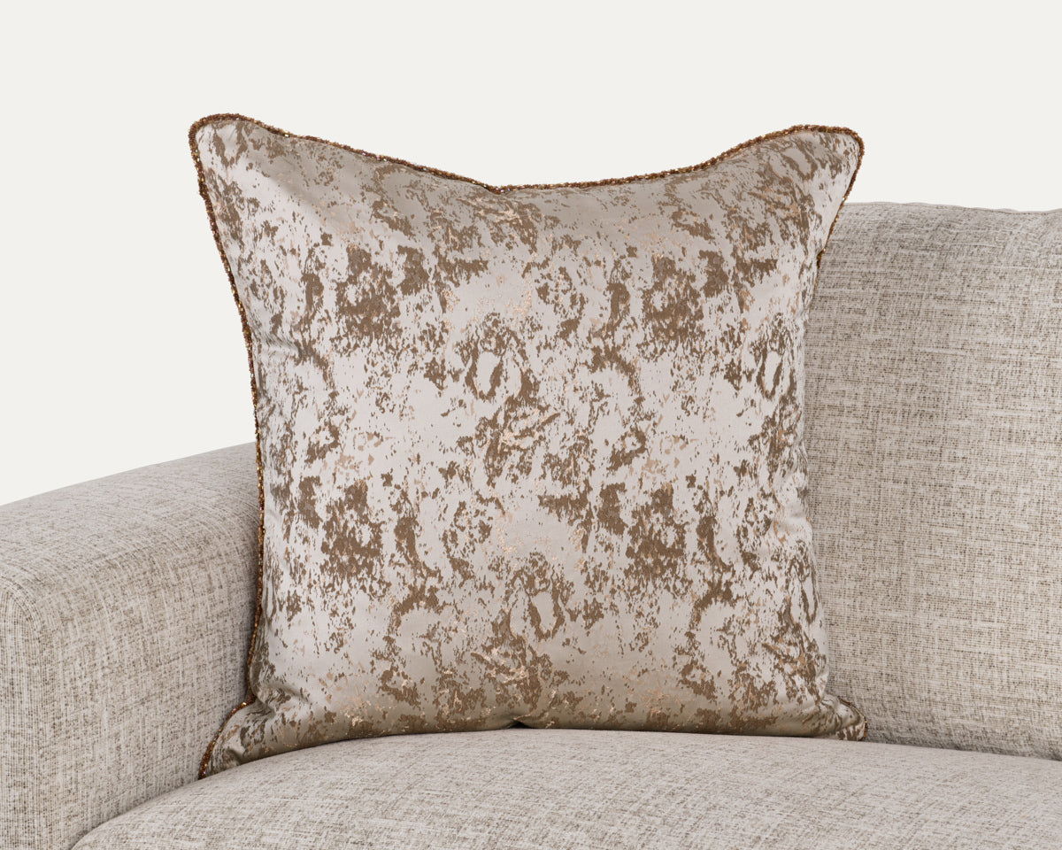 Textured throw pillow with mottled light beige pattern and piped edges, square shape