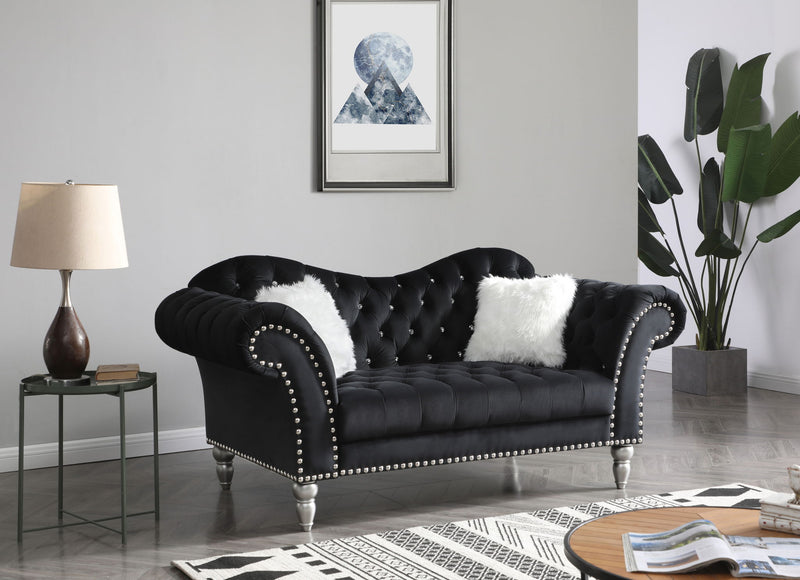 Black tufted round arm loveseat with nailhead trim and two white faux fur pillows.