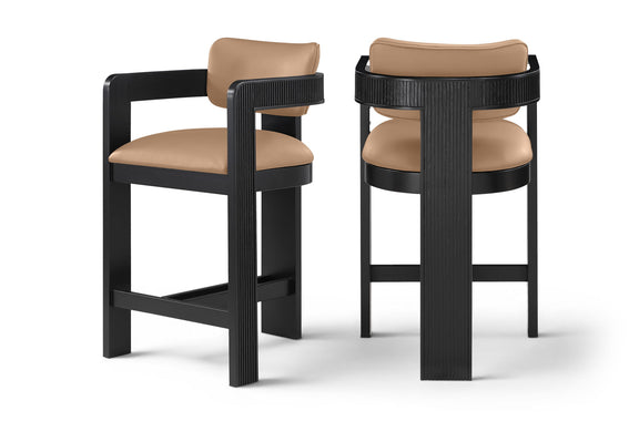 Two vegan leather counter stools with warm tan upholstered seats and black ribbed frames