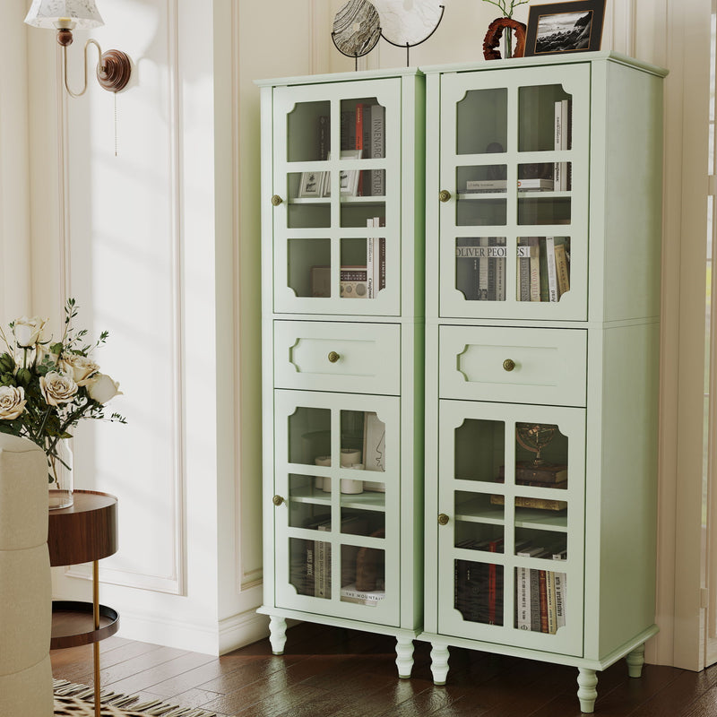 Two pale green curio cabinets with glass grid doors and drawers, displaying books and decor