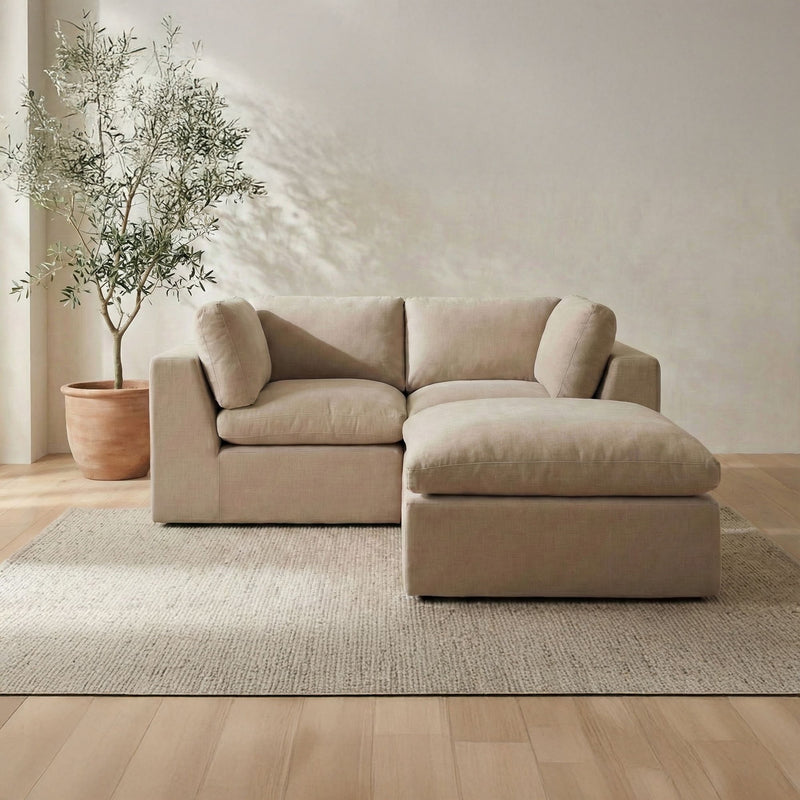 Beige modular sectional sofa with wide armrests and chaise ottoman, soft fabric cushions