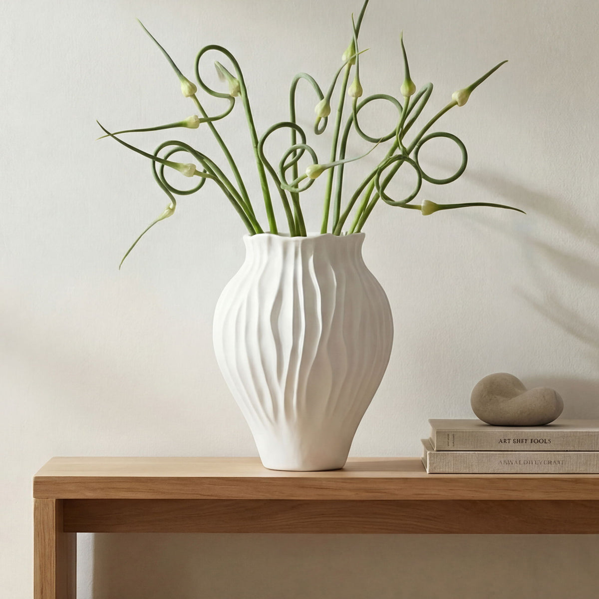 White ribbed ceramic vase holding green stems and buds