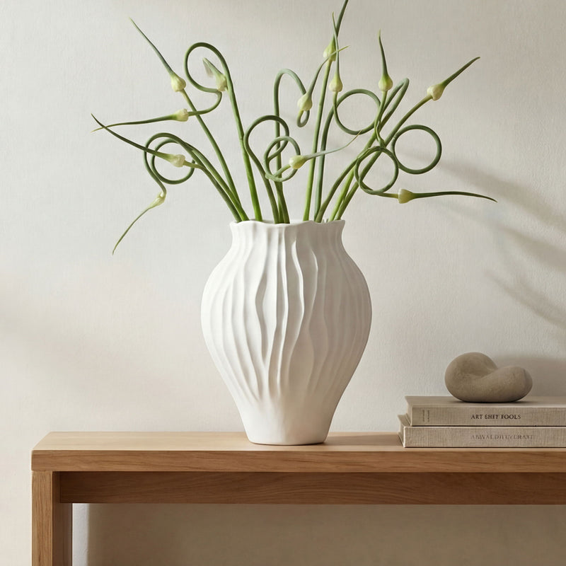 White ribbed ceramic vase holding green stems and buds