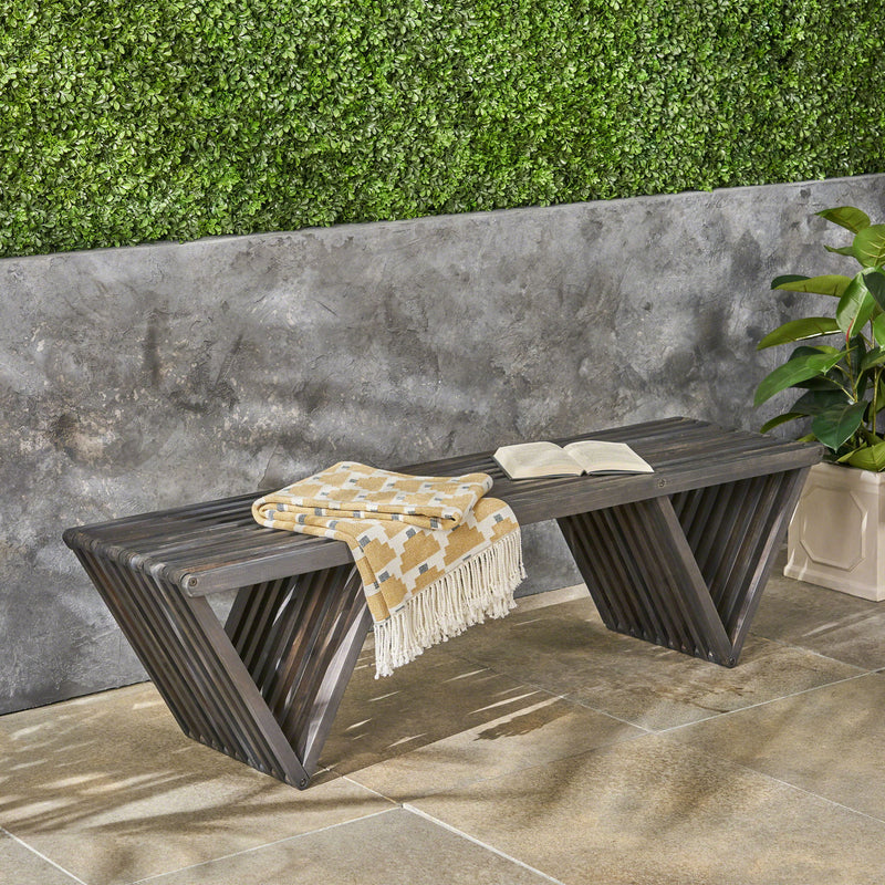 Dark gray slatted outdoor bench with open book and patterned throw blanket
