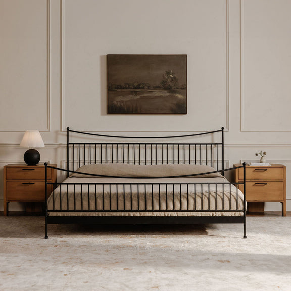 Small dark framed landscape painting above a metal bed with striped bedding