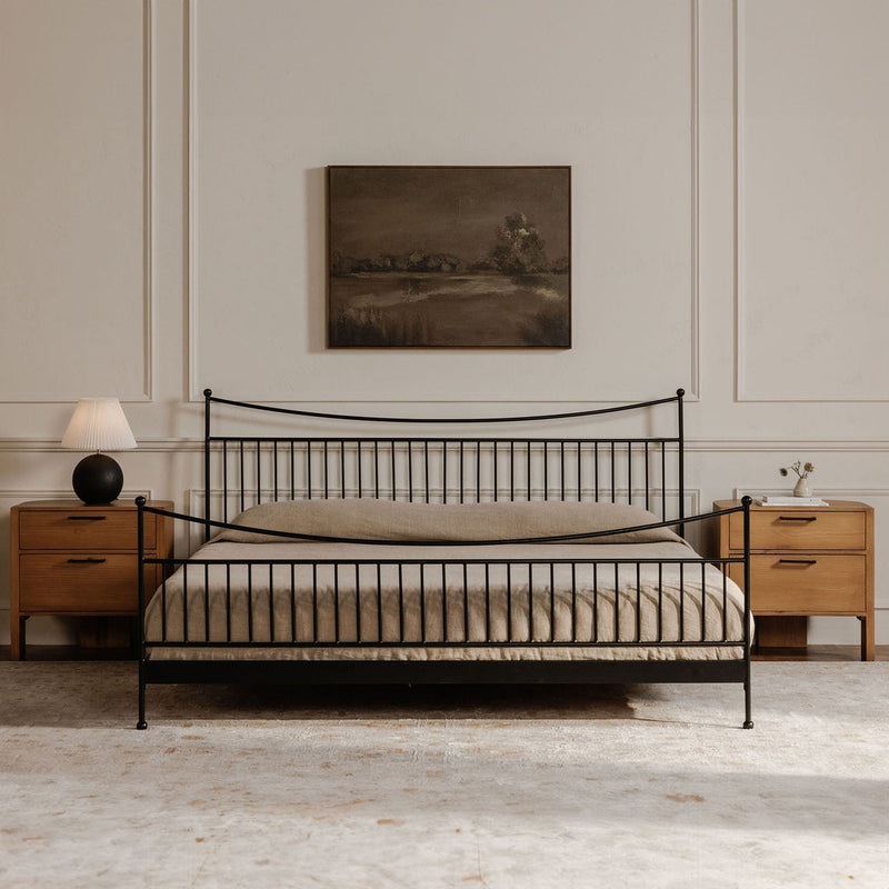 Small dark framed landscape painting above a metal bed with striped bedding