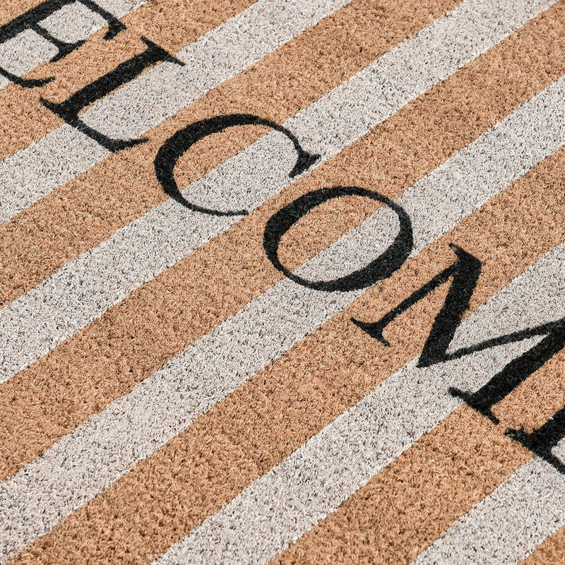 Striped doormat close-up with black 'WELCOME' letters across tan and light stripes