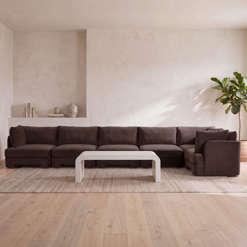 Dark brown velvet L-shaped sectional sofa with chaise section and cushioned armrests.