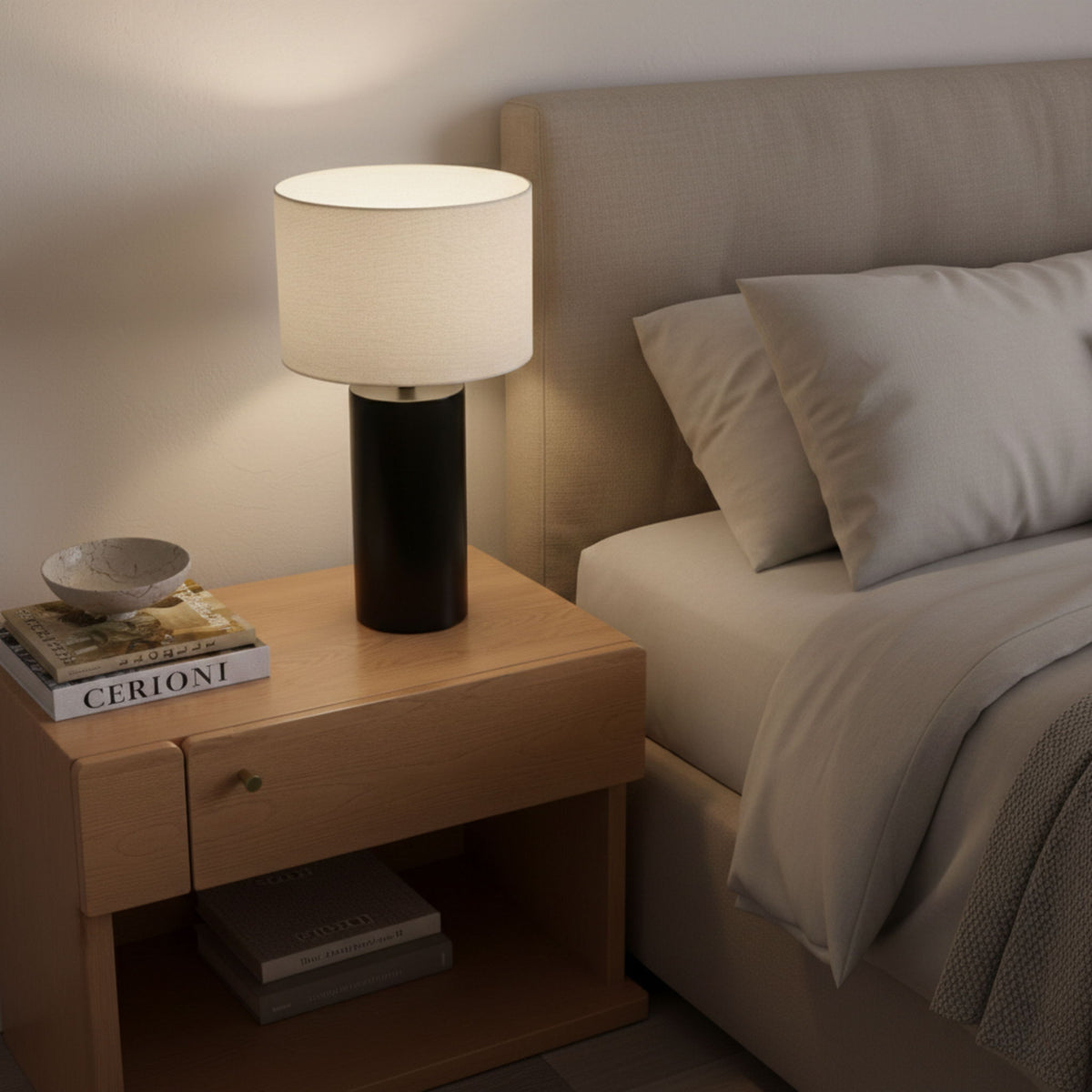 Table lamp with white fabric drum shade and matte black base on nightstand