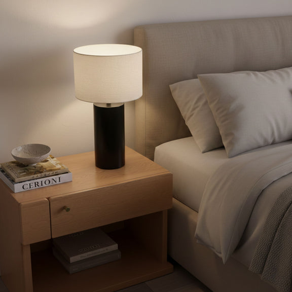 Table lamp with white fabric drum shade and matte black base on nightstand