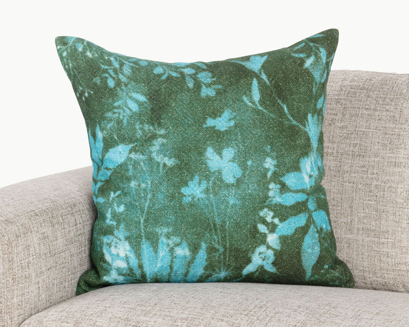 Green botanical throw pillow with blue leaf and flower pattern on sofa
