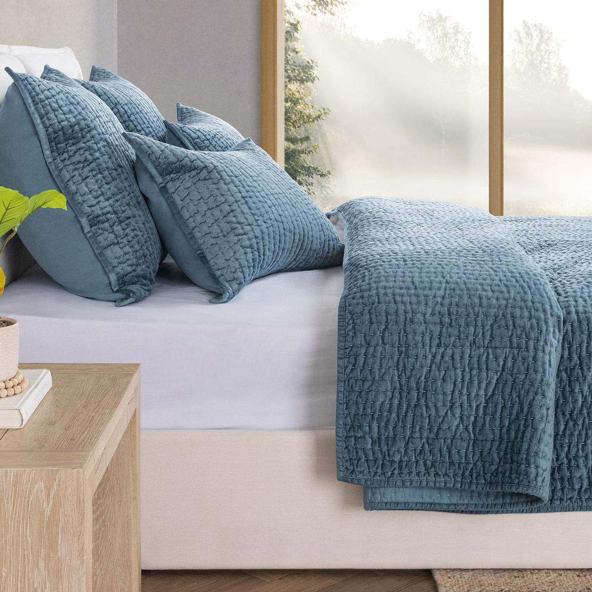 Blue velvet quilt set with textured quilt and coordinating pillow shams on sofa.