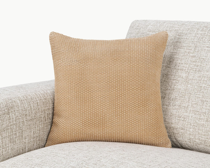 Tan woven square pillow on light upholstered seating