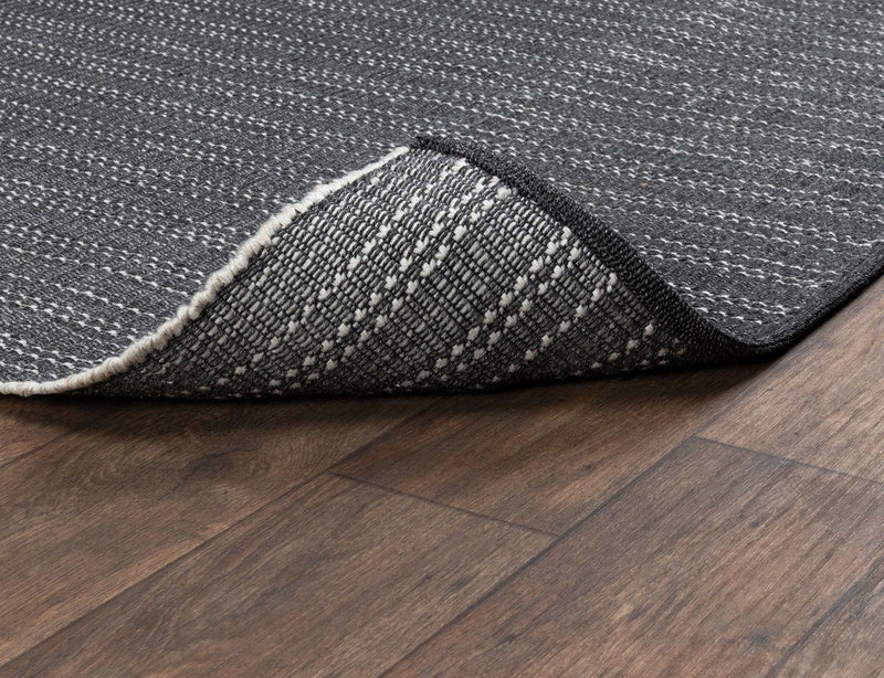 Charcoal indoor/outdoor rug corner detail with flat woven surface and bound edge.
