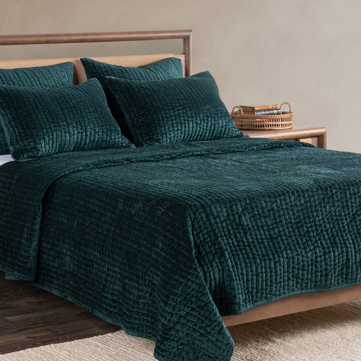 Deep green velvet quilt with matching pillow shams on a wooden bed