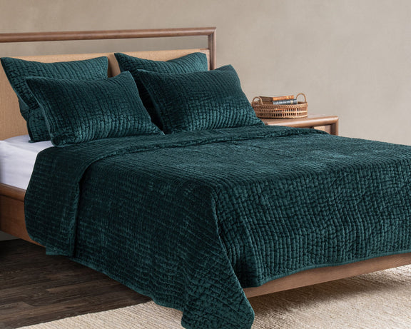 Deep green velvet quilt with matching pillow shams on a wooden bed