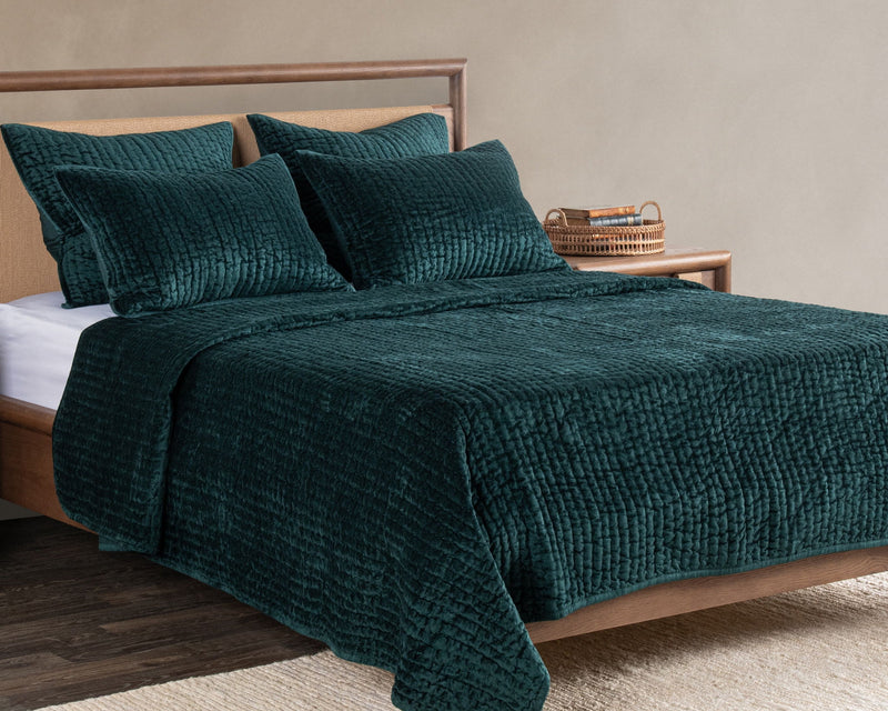 Deep green velvet quilt with matching pillow shams on a wooden bed