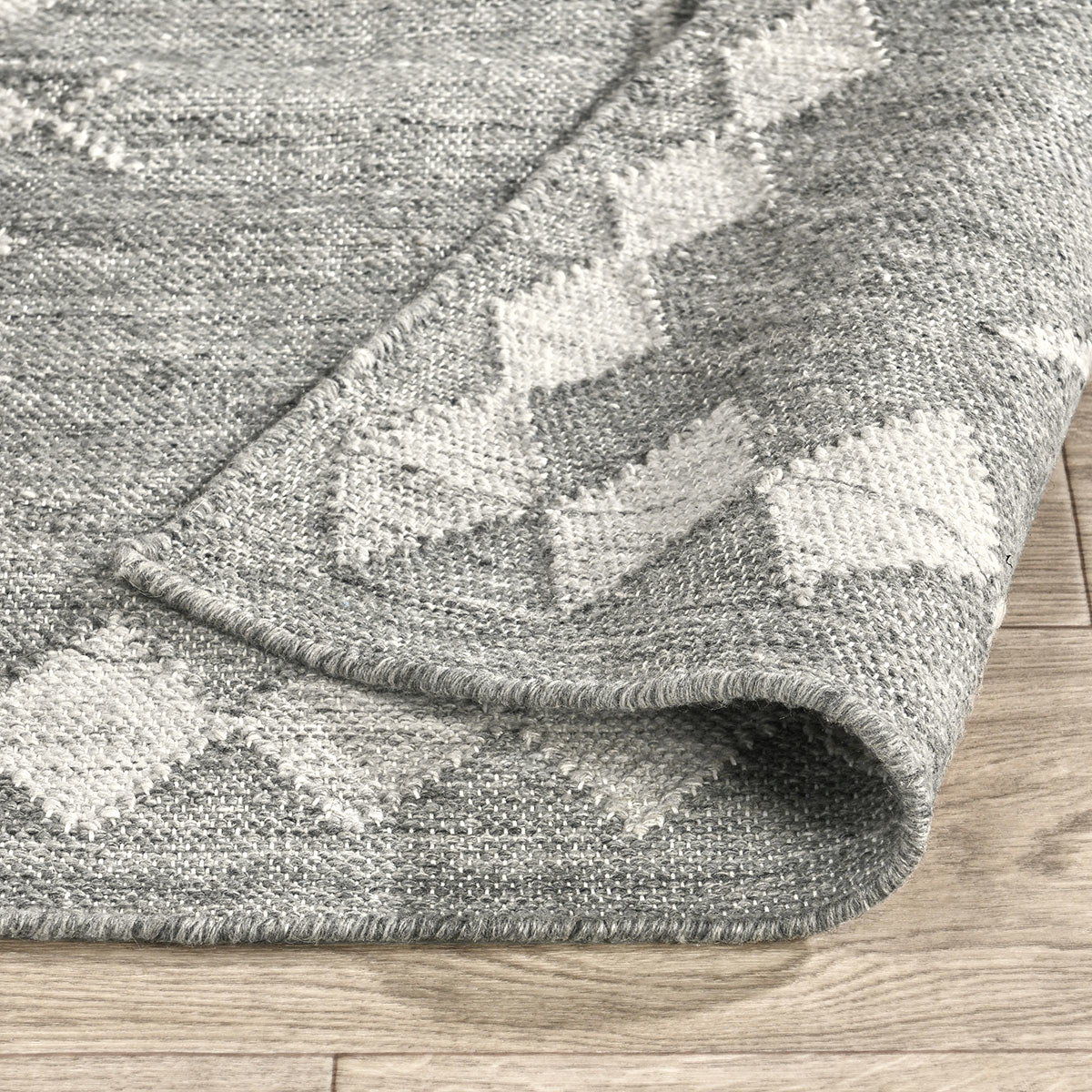 Close-up of gray indoor/outdoor rug edge with cream diamond weave pattern and stitched border