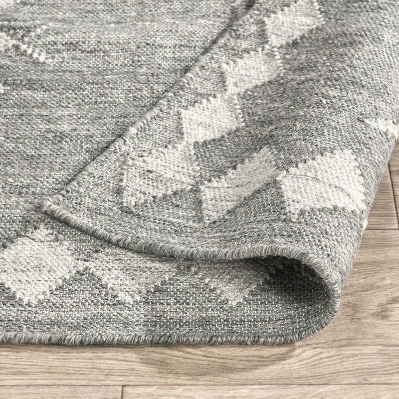Close-up of gray indoor/outdoor rug edge with cream diamond weave pattern and stitched border